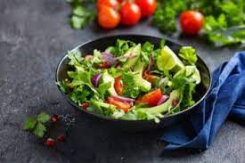 salad with rocket, tomatoes, spinach, lime, onions in a black round bowl