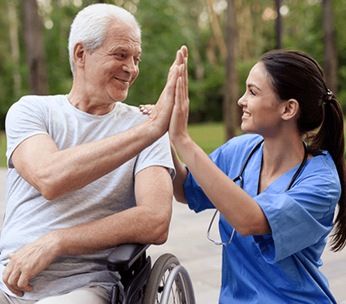 Personal Support Worker giving an elderly man in a wheelchair a high five and is smiling