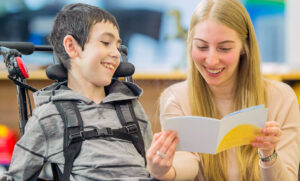 Young Lady reading a book and providing respite care to a small disabled boy